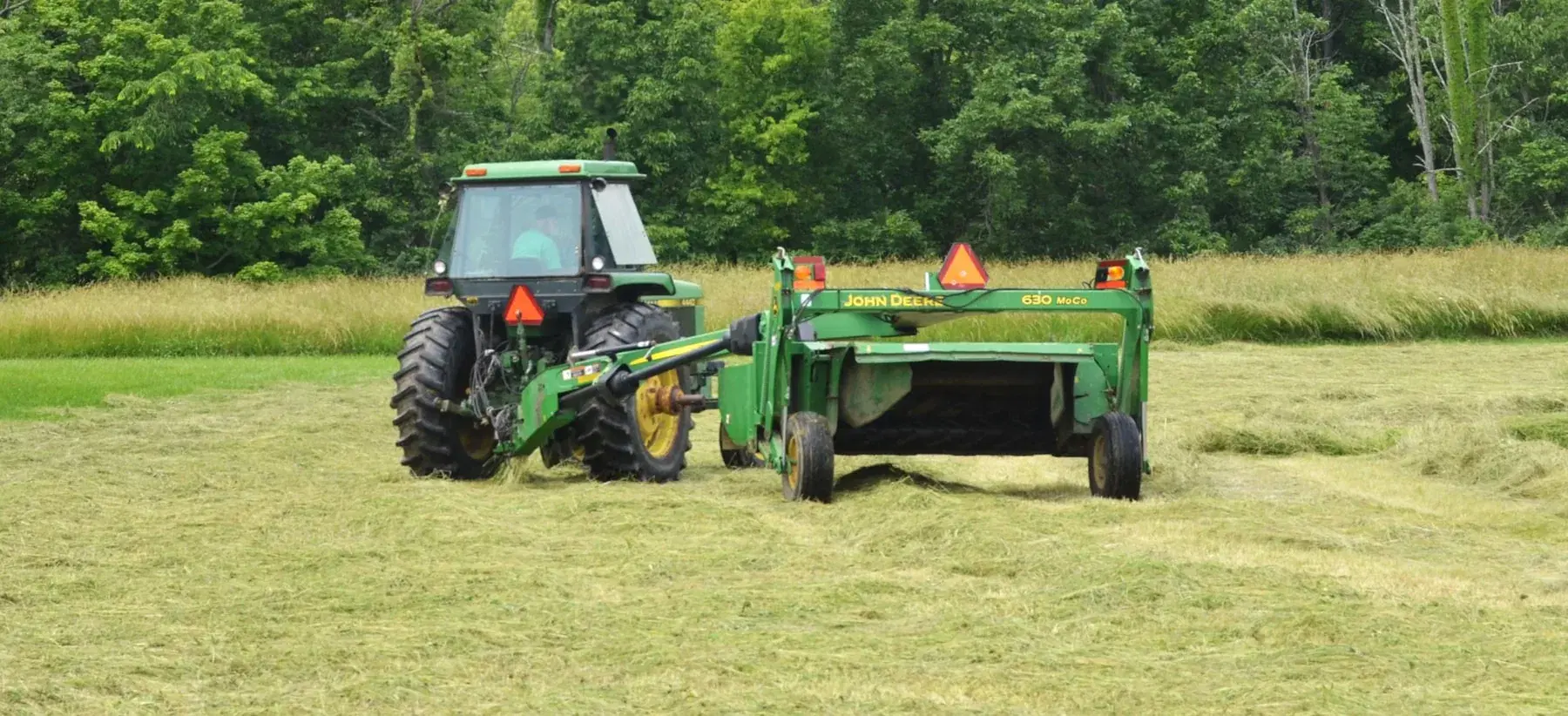 Tractor clearing tall overgrown field grass with heavy duty mowing equipment