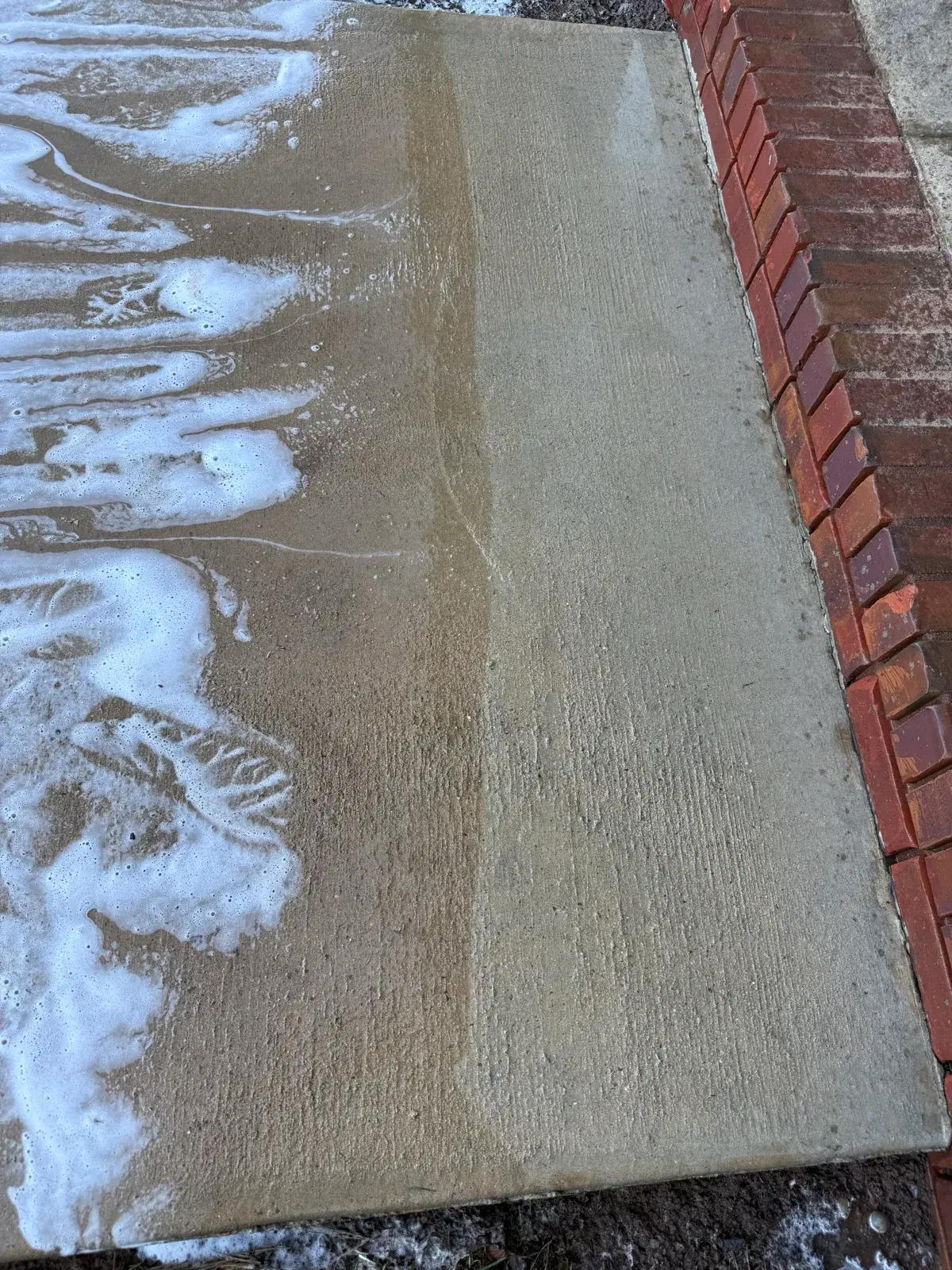 Concrete sidewalk mid clean showing foam and cleaning progress